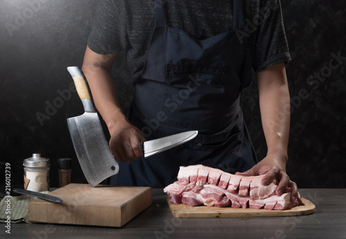 Chef cook cuts large piece of pork meat on wooden cutting board with knife,concept of cooking