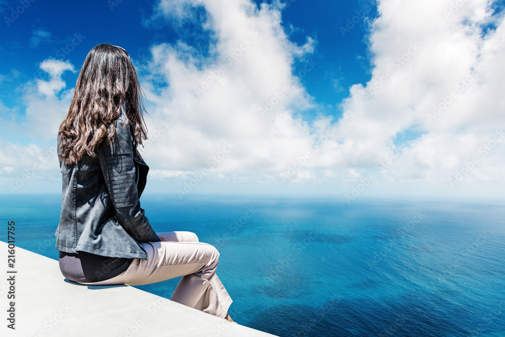 Woman sitting on white platform overlooking ocean