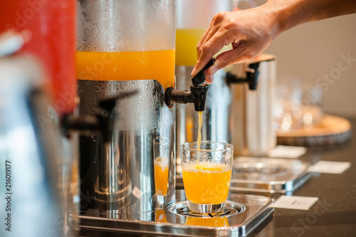 close up hand pulling down the lever of juice dispenser for fresh orange juice.