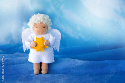 White felt Christmas angel with yellow star in hands on blue silk background,. photo