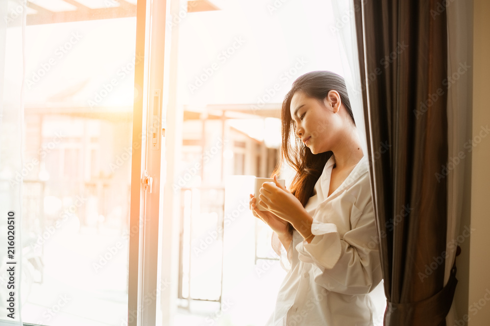 Fototapeta premium Woman holding a cup of coffee in her hands.Woman drinking coffee at home with sunrise at window .