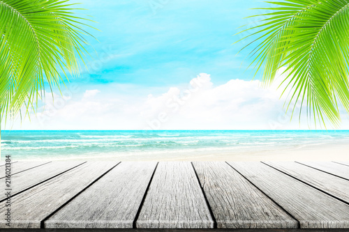 Empty wooden table and palm leaves with party on paradise beach blurred background in summer time.