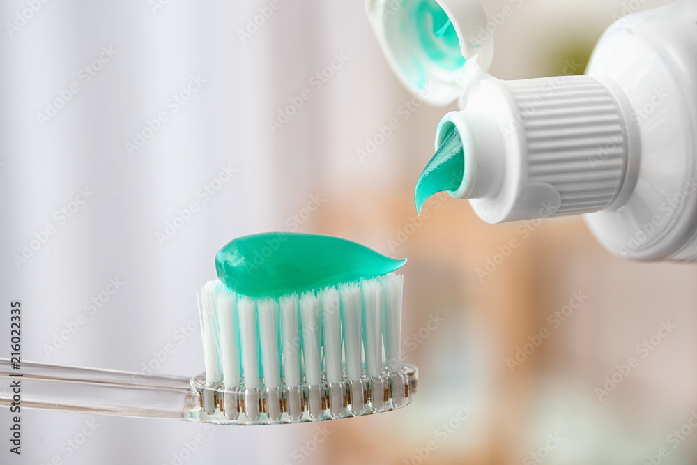 Applying paste on toothbrush against blurred background, closeup Applying paste on toothbrush against blurred background, closeup