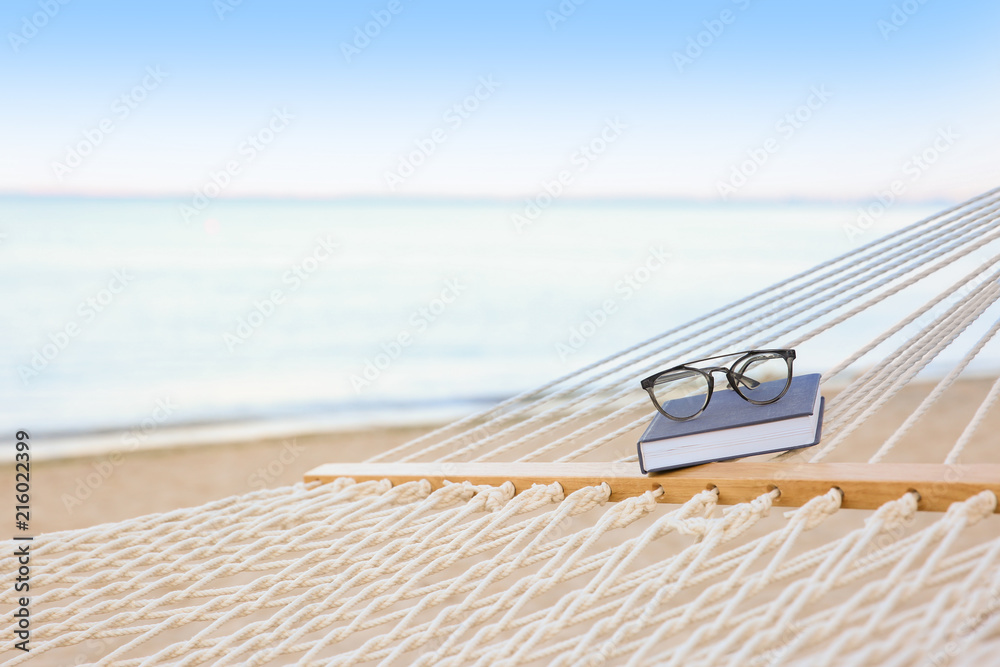 Fototapeta premium Comfortable hammock with book and glasses at seaside
