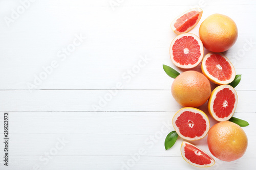 Ripe grapefruits with green leafs on white wooden table