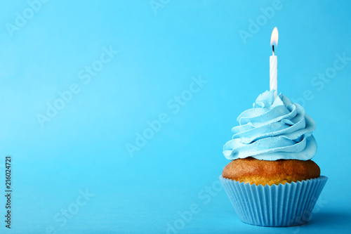 Tasty cupcake with candle on blue background