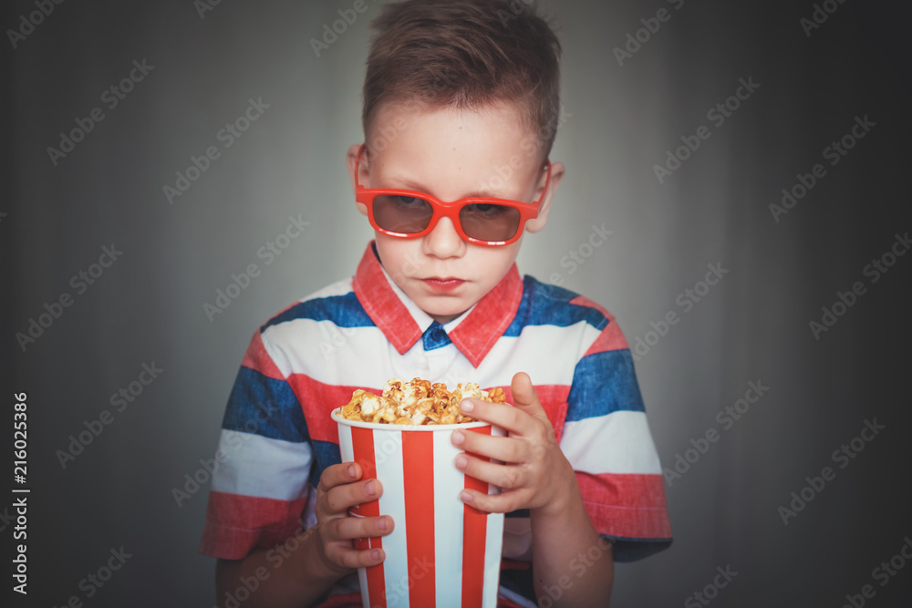 Young boy watch a movie in 3D glasses at the cinema or at home. Little kid eat popcorn over gray background. Home theater. Cute Child in vintage cinema eyeglasses