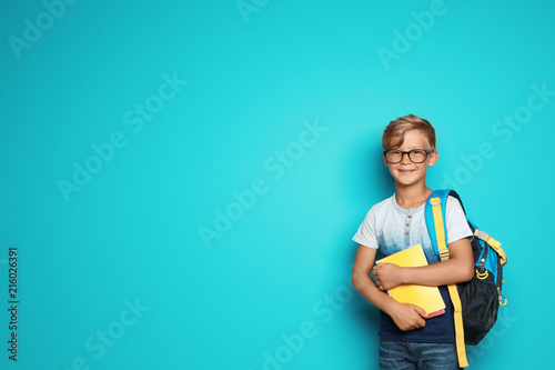 Little school child with backpack and copybooks on color background