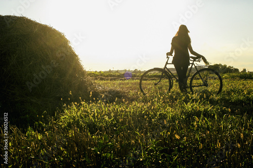 girl silhouette sitting on bicycle in a sunny summer field at sunset