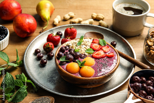Bowl of tasty acai smoothie and ingredients on wooden table