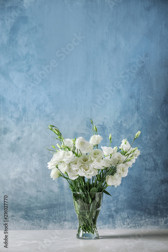 Vase with beautiful Eustoma flowers on table against color background