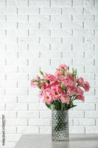 Vase with beautiful Eustoma flowers on table against brick wall