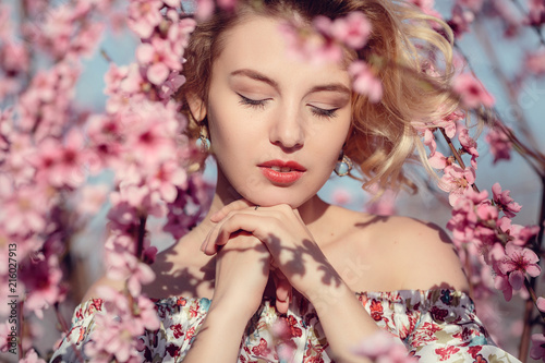 fashion outdoor photo of gorgeous young woman in elegant dress posing in garden with blossom peach trees