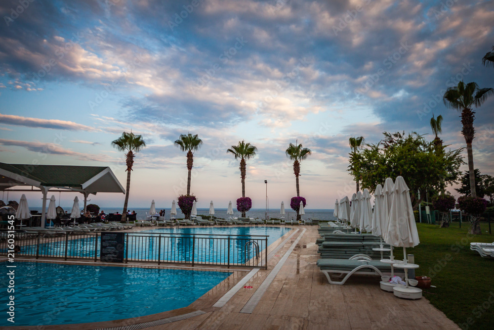 HDR pol view at summer evening in Turkey, with pool, chaise lounges, palms and beauty sky