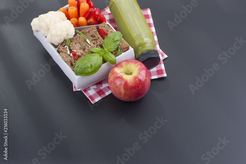 Delicious lunch in a container for school and office. Sandwich, vegetables, apple and green juice for a healthy lunch. Top view on a black background. Copy space.