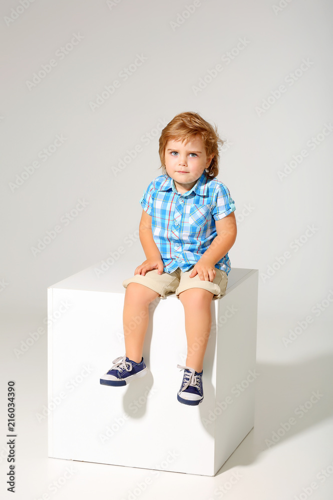 Charming boy in shirt and shorts sitting on a cube