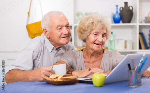 Cheerful mature spouses using laptop at home