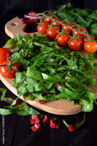 Chopped chard leaves on a cutting board and cherry tomatoes next to it