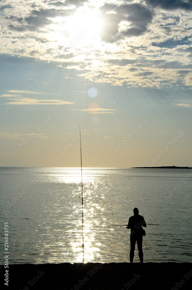Silhouette of fishermen on the quiet sea on late afternoon with sky and sun behind the clouds 