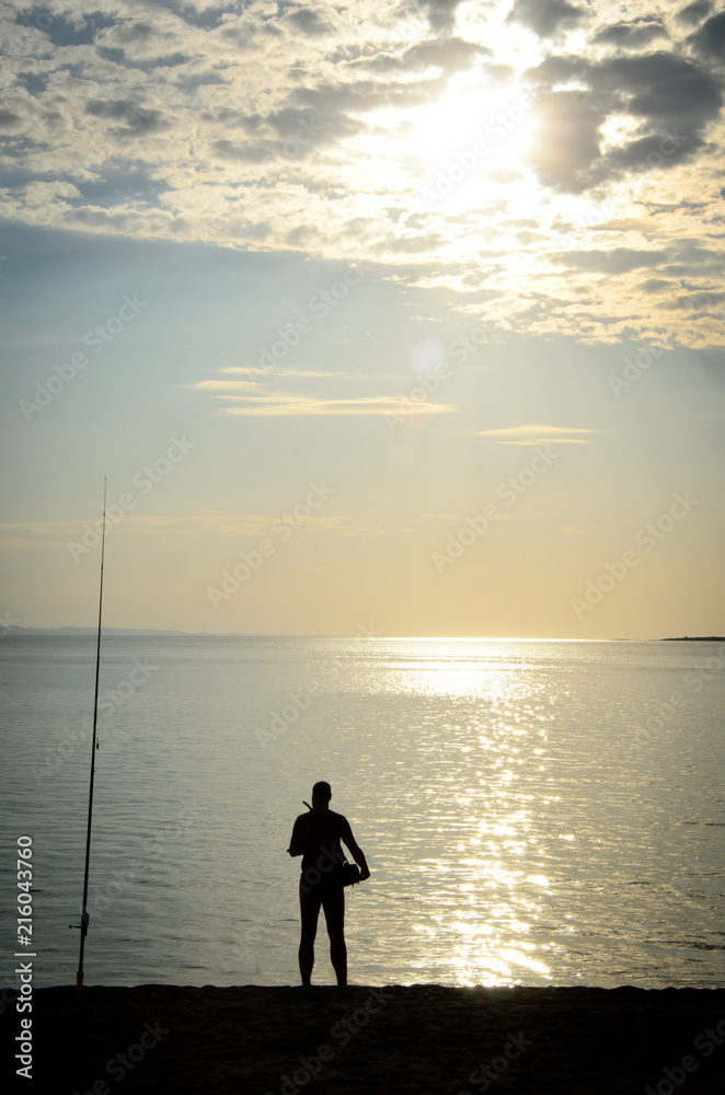 Silhouette of fishermen on the quiet sea on late afternoon with sky and sun behind the clouds 