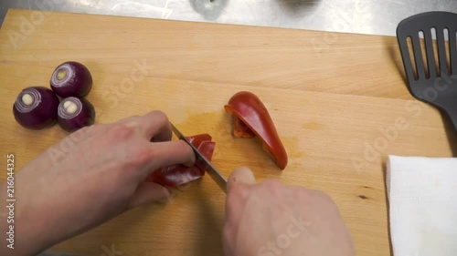 Knife cuts red bell pepper on wooden cutting board. Clip. Cutting core in sweet pepper on wooden cutting board. Remove seeds from red sweet pepper with knife. Preparation of vegetables. Top view. The photo