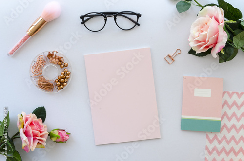 women accessories including blank paper for lettering, notepad, black glasses and roses on white background. beauty concept. Pink color composition, top view