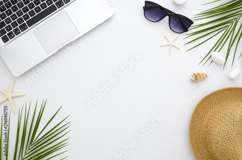 Summer time flat lay. Work and travel concept.Rest, sea, sun, beach and work. Frame from laptop, green leaves, sunglasses and straw hat.