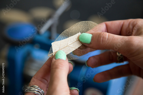 The process of making silver jewellery. Female artist hands close up. Forge-rolling of a siilver blank with a leaf skeleton texture. Crafting a silver ring, see the entire series. photo