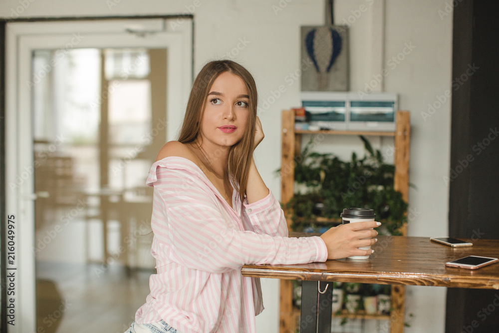 young girl with long straight hair in a pink shirt with bare shoulders drinks coffee in a coffee shop in the summer time young girl with long straight hair in a pink shirt with bare shoulders drinks coffee in a coffee shop in the summer time