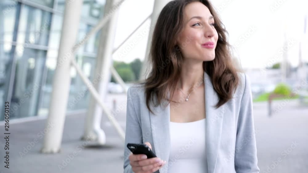 Close up view of Happy and Satisfied Woman Walking in the City. Using her Smartphone. Reading Pleasant Message. Laughing Sincerly. Looking at Mobile’s Screen. Charming Smile. Close up view of Happy and Satisfied Woman Walking in the City. Using her Smartphone. Reading Pleasant Message. Laughing Sincerly. Looking at Mobile’s Screen. Charming Smile.