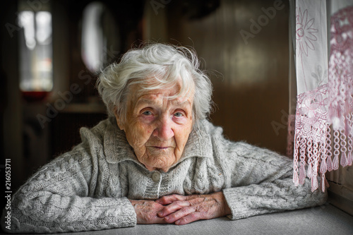 Gray-haired elderly woman sitting near the window.