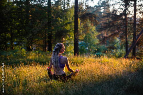 Yoga woman meditates in a clearing in the woods. Peaceful and harmony.