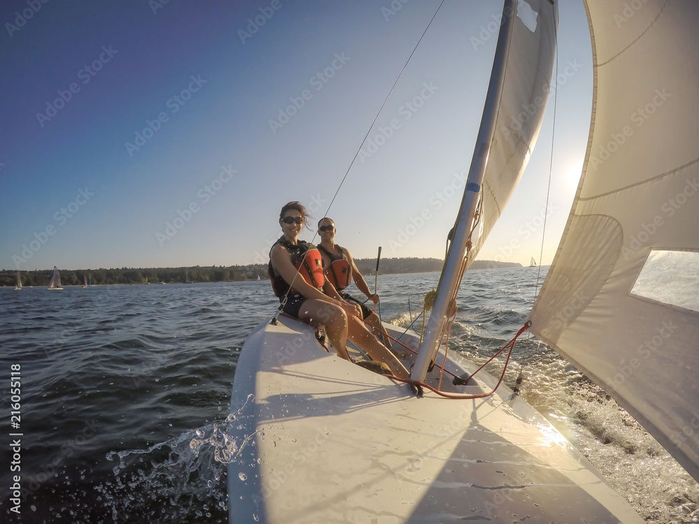 Naklejka premium Couple friends sailing on a small boat in the ocean during a vibrant sunset. Taken near Jericho, Vancouver, BC, Canada.