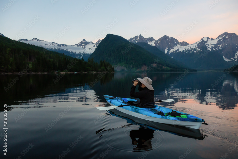 Adventure photographer on a kayak in the water surrounded by the Beautiful Canadian Mountain Landscape. Taken in Jones Lake, near Hope, East of Vancouver, BC, Canada.