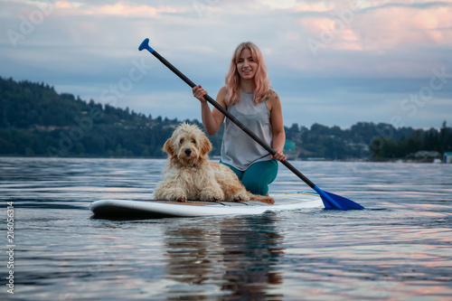Girl with a dog on a paddle board during a vibrant summer sunset. Taken in Deep Cove, North Vancouver, BC, Canada. photo