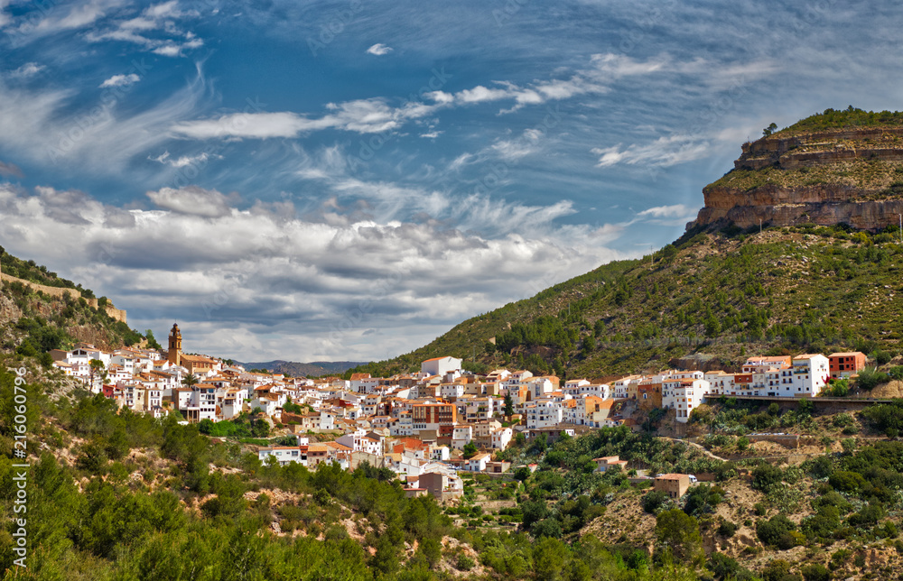 The entire town of Chulilla, Spain in a mountainous canyon area with bright blue sky and clouds as seen from the trails behind it