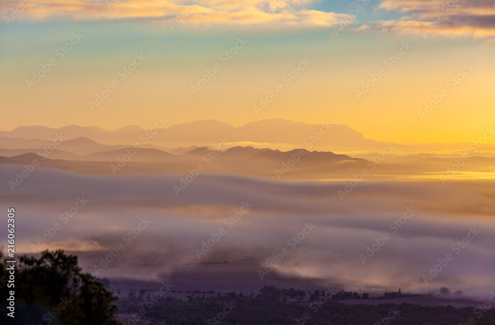 Mountain ridges protruding above low clouds at vivid sunset in Australia