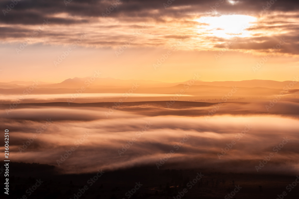 Mountain peaks protruding through low clouds at beautiful sunrise
