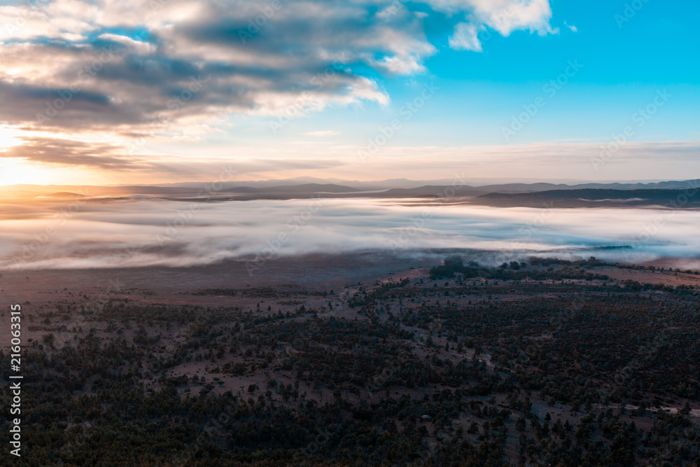 Low clouds over land, mountains, and trees at sunrise