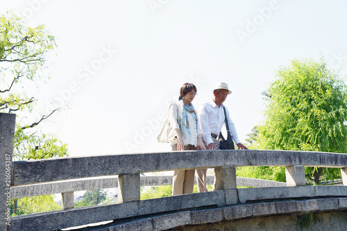 旅先の観光地の橋の上で、川を眺めるシニア夫婦