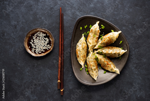 Fried dumplings Gyoza in plate, soy sauce, and chopsticks on a black concrete background, top view