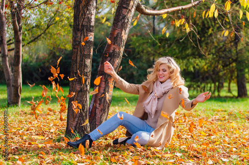 Young beautiful woman throwing up fallen autumn leaves over her head