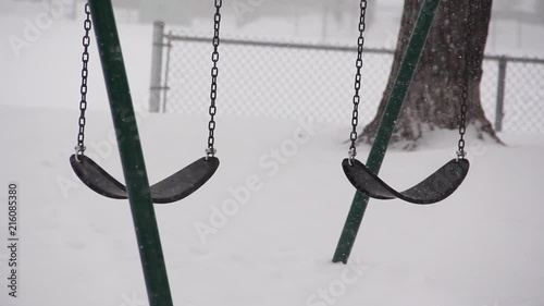Two swings sway back in forth in the snowy blizzard. No kids are in the park enjoying the cold weather. Location: Winnipeg, Manitoba. photo
