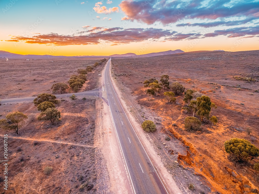 Rural road leading to the hills through desert at sunset - aerial view