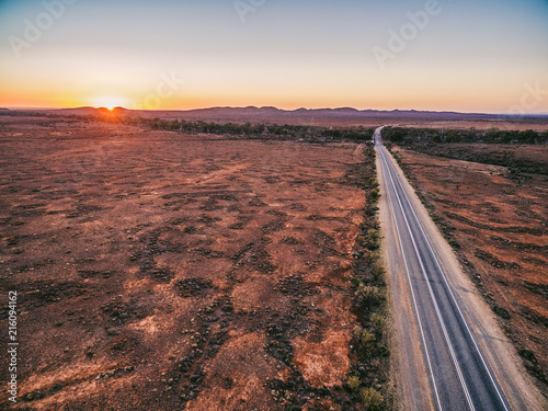 Road passing through Australian outback leading to Flinders Ranges peaks at sunset