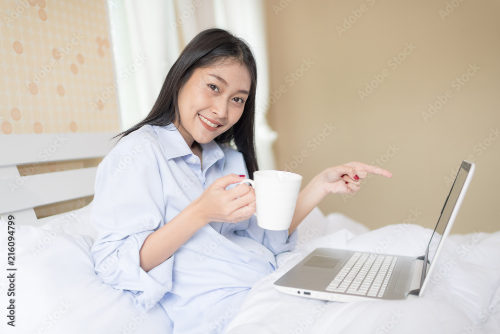 Excited woman with laptop sitting on bed in morning sunlight. Have a nice day concept.