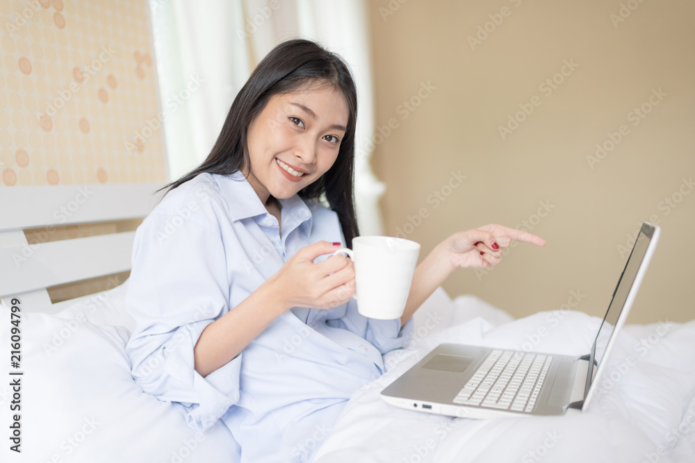 Excited woman with laptop sitting on bed in morning sunlight. Have a nice day concept. Excited woman with laptop sitting on bed in morning sunlight. Have a nice day concept.