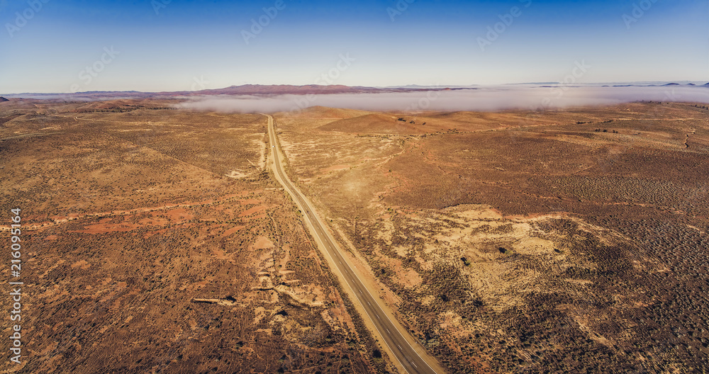 Countryside highway passing through Australian outback desert leading to mountains - aerial panorama