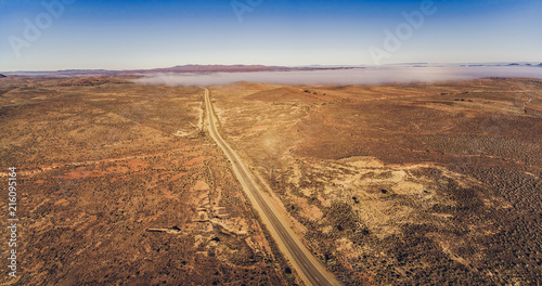 Countryside highway passing through Australian outback desert leading to mountains - aerial panorama photo