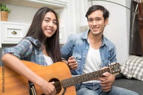 In selective focus of Young beautiful couple resting at home and playing guitar.Woman learning to playing a song.